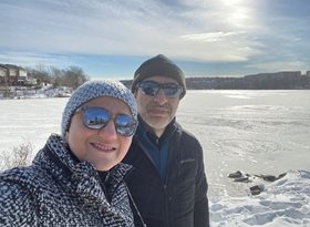 A man and a woman standing outside in the wintertime with a frozen pond behind them