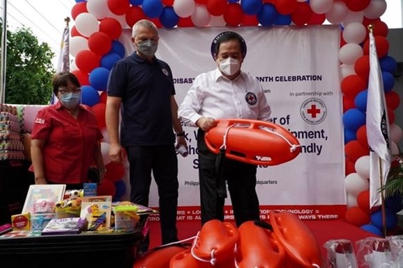 Philippine Red Cross members are on stage, while one holds up an emergency kit item during the handover ceremony