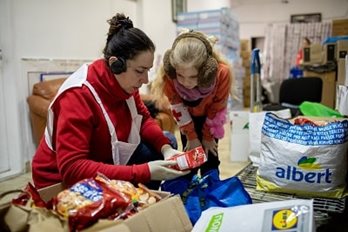 A woman and young girl in a supply room at an open box full of food supplies
