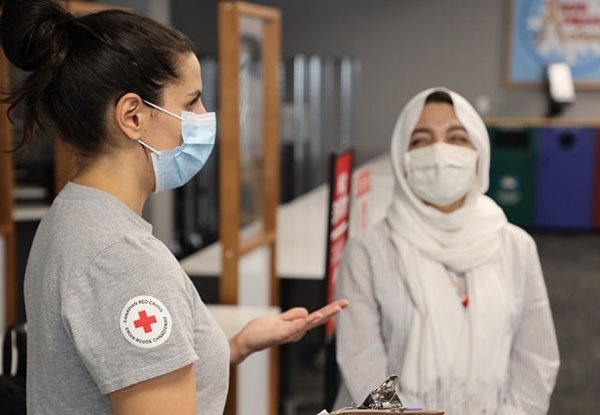 Two women in masks, one wearing a Canadian Red Cross shirt, talking to each other