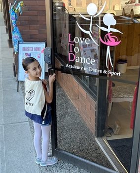 A young girl opening the door to the Love to Dance Academy looking over her shoulder and smiling