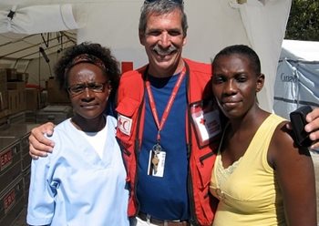 Guy standing with two women in front of a Red Cross supplies tent in Haiti