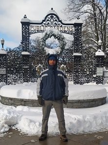 A man standing in front of wrought iron gates covered in snow