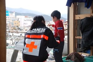 A Japanese Red Cross team member with a small child looking out at the destruction left by a tsunami in March 2011