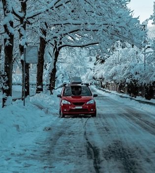 A car driving on a wintry road surrounded by snow-covered trees.
