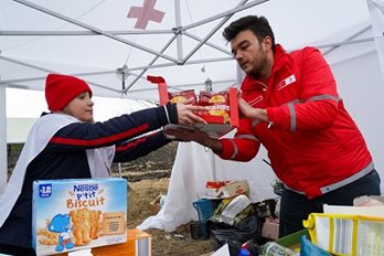 Two Red Cross members handing boxed food to each other in a white Red Cross tent