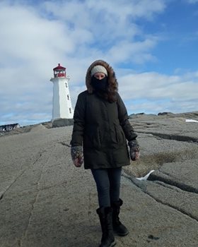 A woman in winter coat, scarf and hat standing in front of a lighthouse in Peggy's Cove, NS.