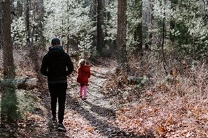An adult walking slightly behind a young girl down a path through the woods