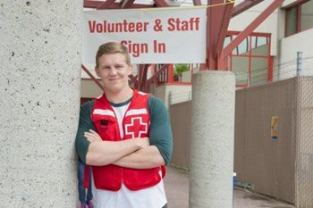 Canadian Red Cross Jack McCaskill leaning against a pillar in front of a sign that says Volunteer & Staff Sign In