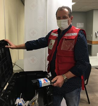 A man standing by an open suitcase with a mask on and wearing a Red Cross vest.