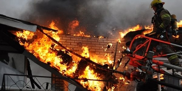 A house on fire with a firefighter on a ladder