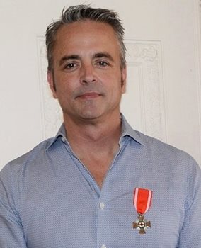 A headshot of a man wearing the Order of the Red Cross medal pinned to his shirt