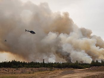 An helicopter flies across wildfire smoke in the Northwest Territories