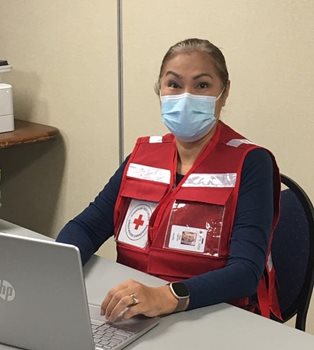 A woman in a Red Cross vest sitting at a desk, smiling