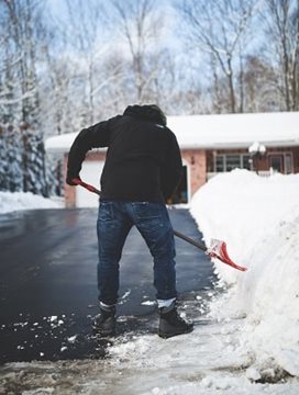 A person shovelling a driveway to a house