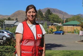 Zaineb smiling in a Red Cross vest with mountains in the background.