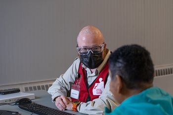 William Coney, dressed in a Red Cross vest and wearing PPE, is discussing with a person affected by Fiona