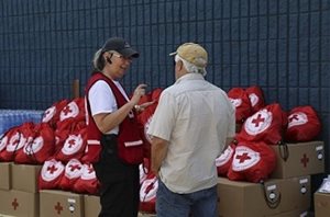 A Red Cross worker helping provide residents with clean-up kits which are lined up against a wall.