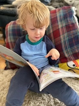 A toddler sitting on a couch reading a book