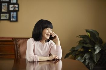 A woman sitting at a dining room table holding a phone to her ear