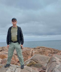 Joe Michielsen is standing on rocks, in front of the sea