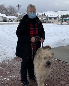 Barb standing in a mask outside with snow around, holding the leash to her dog, Daisy