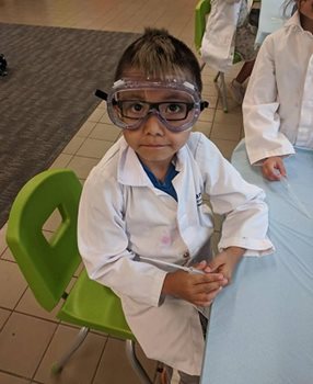 A young boy in goggles and a white lab coat.