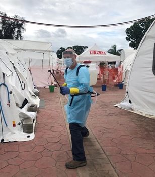 Garry in full PPE gear and spray can standing among white tents, one with ERU on it