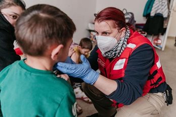 A woman in Red Cross vest looking at a child