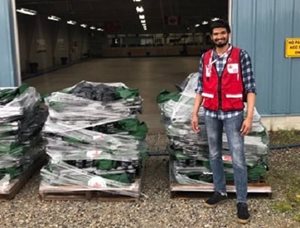Ashwin, in a Red Cross vest, standing outside a warehouse in front of supplies