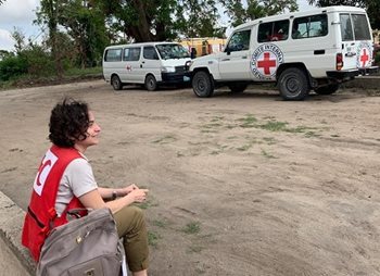 Lucia sitting on a curb beside a Red Cross van