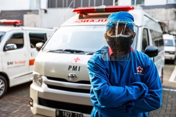A man in mask and goggles standing in front of an ambulance