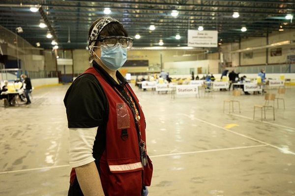A woman in mask and goggles standing inside an arena where chairs and tables are set up